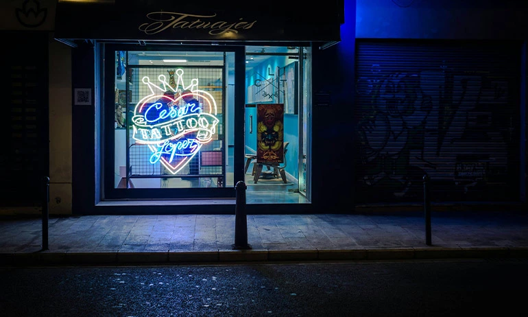 A tattoo shop front lit by a neon sign at night.