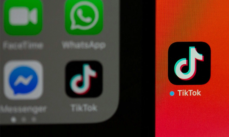 A close-up photo showing a smartphone screen with various app icons, prominently featuring the TikTok app icon in focus with other blurred icons in the background.