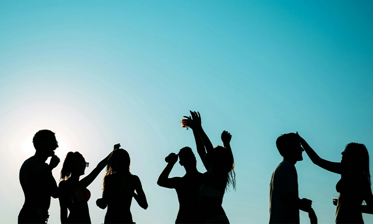 Silhouette of friends dancing and having fun at the beach with a clear blue sky in the background.